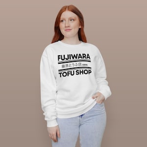 May include: White sweatshirt with the text "FUJIWARA" above Japanese characters and "TOFU SHOP" in black. The sweatshirt is worn by a person wearing blue jeans.