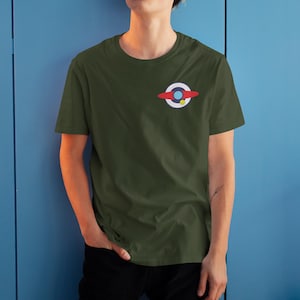 Puede incluir: Camiseta verde oliva con un peque&ntilde;o gr&aacute;fico colorido en el pecho izquierdo. El gr&aacute;fico presenta un c&iacute;rculo blanco con un centro azul, una forma curva roja y un punto amarillo. La camiseta es de manga corta y cuello redondo.