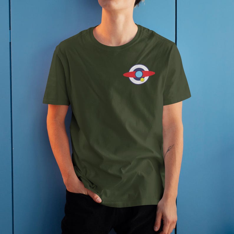 Puede incluir: Camiseta verde oliva con un peque&ntilde;o gr&aacute;fico colorido en el pecho izquierdo. El gr&aacute;fico presenta un c&iacute;rculo blanco con un centro azul, una forma curva roja y un punto amarillo. La camiseta es de manga corta y cuello redondo.