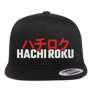 May include: Black trucker hat with a white mesh back. The front of the hat has the Japanese characters "ハチロク" in red and the English words "HACHI ROKU" in white.