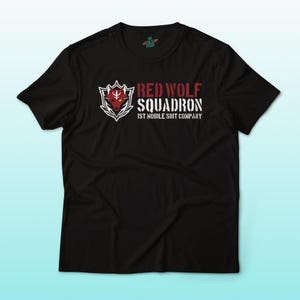 May include: Black t-shirt featuring a graphic design with the text "RED WOLF SQUADRON" in white and red. The design includes a wolf head within a shield. The text "1ST MOBILE SUIT COMPANY" is also present.