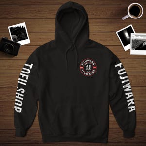 May include: Black hooded sweatshirt with white text on the sleeves that reads "FUJIWARA" and "TOFU SHOP". The front of the sweatshirt has a red and white circle with the text "FUJIWARA TOFU SHOP AE 86" inside.