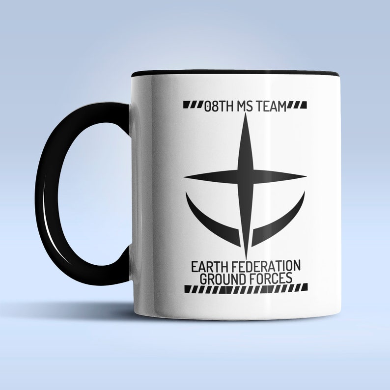 Puede incluir: Taza de cer&aacute;mica blanca con asa y borde negros. La taza presenta un gr&aacute;fico en blanco y negro de una cruz estilizada con una forma de media luna alrededor. El texto "08TH MS TEAM" y "EARTH FEDERATION GROUND FORCES" est&aacute; impreso en negro en la taza.