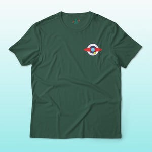 Puede incluir: Camiseta verde oscuro con un peque&ntilde;o gr&aacute;fico colorido en el pecho. El gr&aacute;fico presenta un dise&ntilde;o rojo, blanco, azul y amarillo. La camiseta est&aacute; hecha de un material suave y tiene mangas cortas.