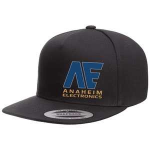 May include: A black flat-brimmed baseball cap with the text "AE ANAHEIM ELECTRONICS" in blue and gold. The cap has a snapback closure and a classic design.