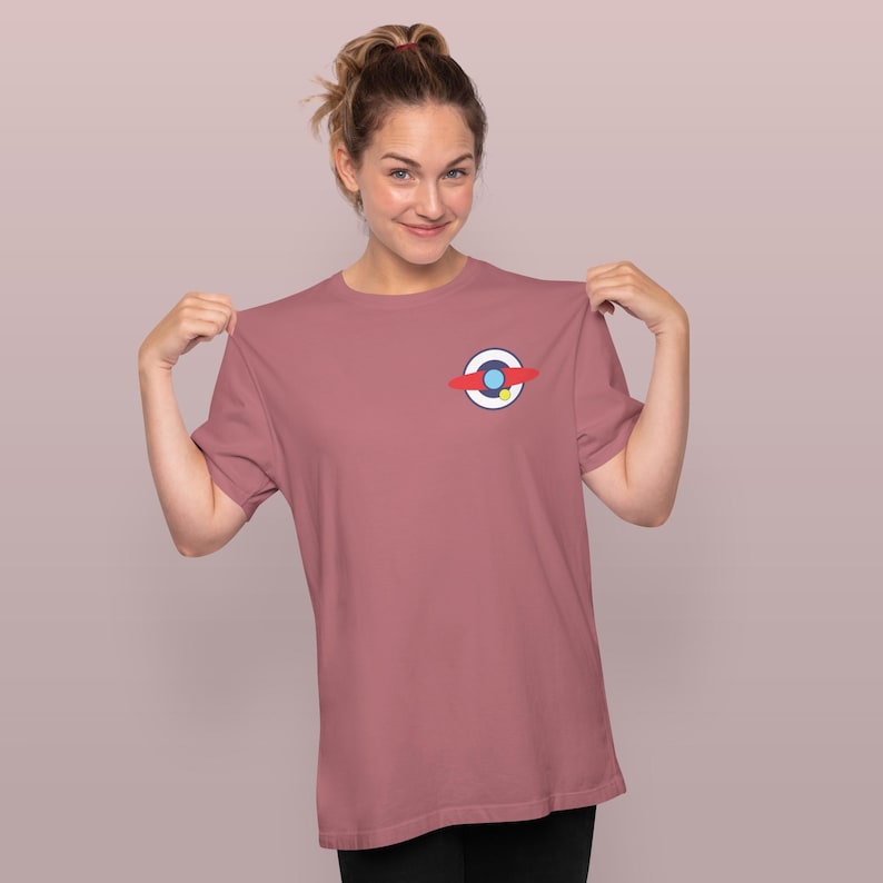 Puede incluir: Camiseta rosa polvoriento con un peque&ntilde;o gr&aacute;fico en el pecho. El gr&aacute;fico es un c&iacute;rculo con una franja roja, un c&iacute;rculo azul y un punto amarillo. La camiseta es de color liso y tiene mangas cortas.