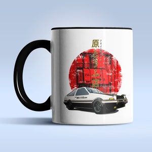 May include: White ceramic mug with a black handle. The mug features a white car with a red and white Japanese flag in the background. The car has black and white stripes and the text "藤原豆腐店" in Japanese.