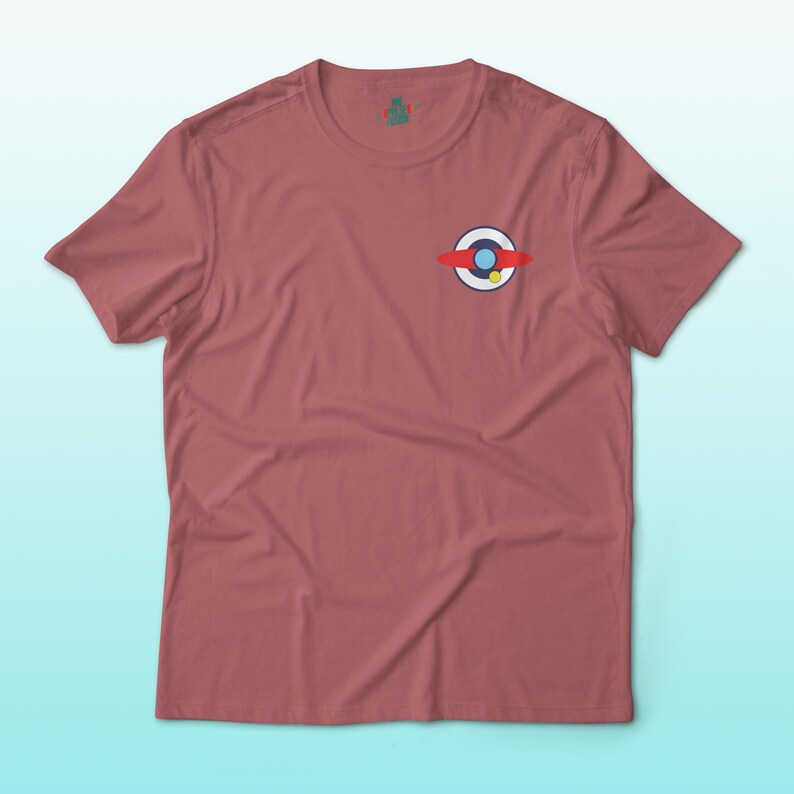 Puede incluir: Una camiseta de color rosa polvoriento con un peque&ntilde;o gr&aacute;fico colorido en el pecho izquierdo. El gr&aacute;fico presenta un c&iacute;rculo blanco con un c&iacute;rculo azul en el interior, una banda roja y un punto amarillo. La camiseta tiene mangas cortas y cuello redondo.