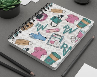 Könnte beinhalten: Ein weißes Spiralnotizbuch mit einem bunten Muster aus medizinischen Gegenständen, darunter ein Stethoskop, ein Verband, eine Kaffeetasse und die Buchstaben "RN".
