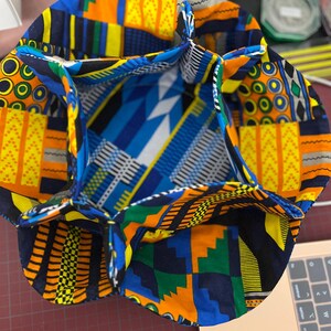 Puede incluir: Un organizador de almacenamiento de tela colorido con múltiples compartimentos. La tela es una mezcla vibrante de amarillo, naranja, azul, verde y negro con patrones geométricos.