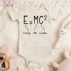 May include: A white baby onesie with black text that reads "E=MC2" with arrows pointing to the words "Energy", "Milk", and "Cuddles".