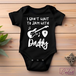 May include: Black baby onesie with white text that reads "I can't wait to jam with Daddy" and a graphic of a guitar, musical notes, and a guitar pick.