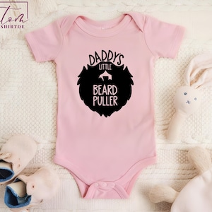 May include: Pink baby onesie with black text that reads "Daddy's Little Beard Puller" and a black silhouette of a beard.