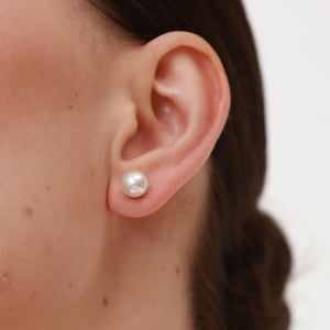 May include: A close-up of a person's ear with a white pearl stud earring.