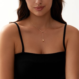 Puede incluir: Un collar de cadena de oro con un colgante en forma de l&aacute;grima. El collar lo lleva una persona con un top negro de tirantes.