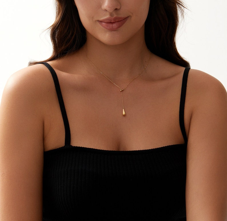 Puede incluir: Un collar de cadena de oro con un colgante en forma de l&aacute;grima. El collar lo lleva una persona con un top negro de tirantes.