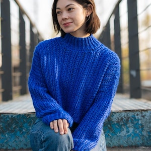 May include: A woman wearing a blue knitted sweater and blue jeans sits on a set of metal stairs.