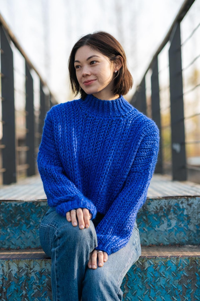 May include: A woman wearing a blue knitted sweater and blue jeans sits on a set of metal stairs.