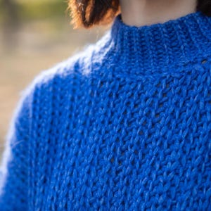 May include: A close-up of a blue knitted sweater with a high neck. The sweater is made of a soft, textured yarn.