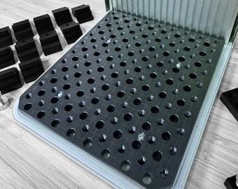 Puede incluir: Un instrumento de laboratorio negro y plateado con una rejilla de agujeros, etiquetados con números y letras. El dispositivo tiene un ventilador y está abierto, revelando el interior. Varios bloques rectangulares negros están dispuestos cerca.