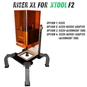 Könnte beinhalten: Ein Riser XL für xTool F2 Lasermaschinen mit einer transparenten orangefarbenen Schutzabdeckung, einem Metallfuß mit vier Beinen und Text, der vier Konfigurationsoptionen einschließlich Höhenadapter und Ausrichtungswerkzeug auflistet.