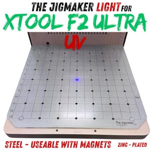 Puede incluir: Placa metálica plateada con un patrón de cuadrícula, diseñada para XTOOL F2 ULTRA. Los textos "THE JIGMAKER LIGHT" y "XTOOL F2 ULTRA" son visibles. La placa está etiquetada como "STEEL - USEABLE WITH MAGNETS ZINC-PLATED".