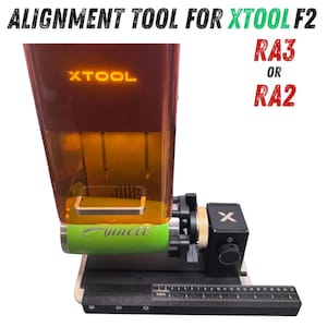 May include: An alignment tool for XTool F2, RA3 or RA2. The tool has a red and clear housing with the XTool logo illuminated in orange. The tool has a green cylindrical component with the name "Anneti" and a black base with a ruler.