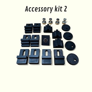 May include: Accessory kit 2 includes black plastic parts, including small rectangular blocks, round discs, and a square magnet. There are also four silver metal push pins.