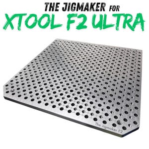 May include: A silver metal jig plate with numerous evenly spaced holes. The text "THE JIGMAKER FOR XTOOL F2 ULTRA" is in green and black above the plate. The text "The Jigmaker F2" is in the bottom right corner.