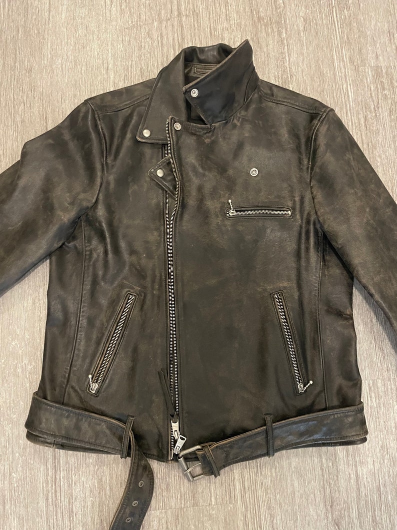 May include: A dark brown leather motorcycle jacket with a zipper closure, a belt, and multiple pockets.