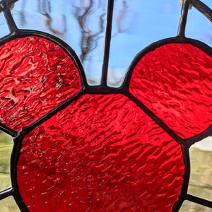 Może przedstawiać: Szklane okno z witrażem przedstawiające czerwoną głowę Myszki Miki. Szkło jest fakturowane i ma lekko tęczowy charakter.