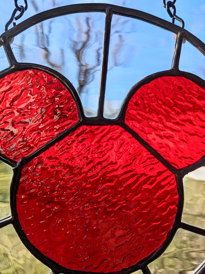 Może przedstawiać: Szklane okno z witrażem przedstawiające czerwoną głowę Myszki Miki. Szkło jest fakturowane i ma lekko tęczowy charakter.