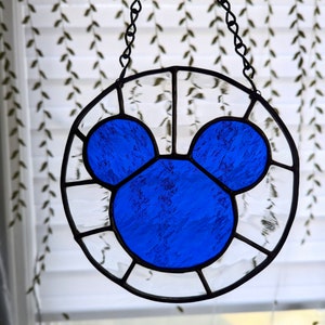 Może przedstawiać: Szklane okno w witrażu wiszące na łańcuchu, przedstawiające niebieską sylwetkę Myszki Miki.