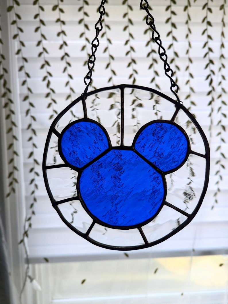 Może przedstawiać: Szklane okno w witrażu wiszące na łańcuchu, przedstawiające niebieską sylwetkę Myszki Miki.