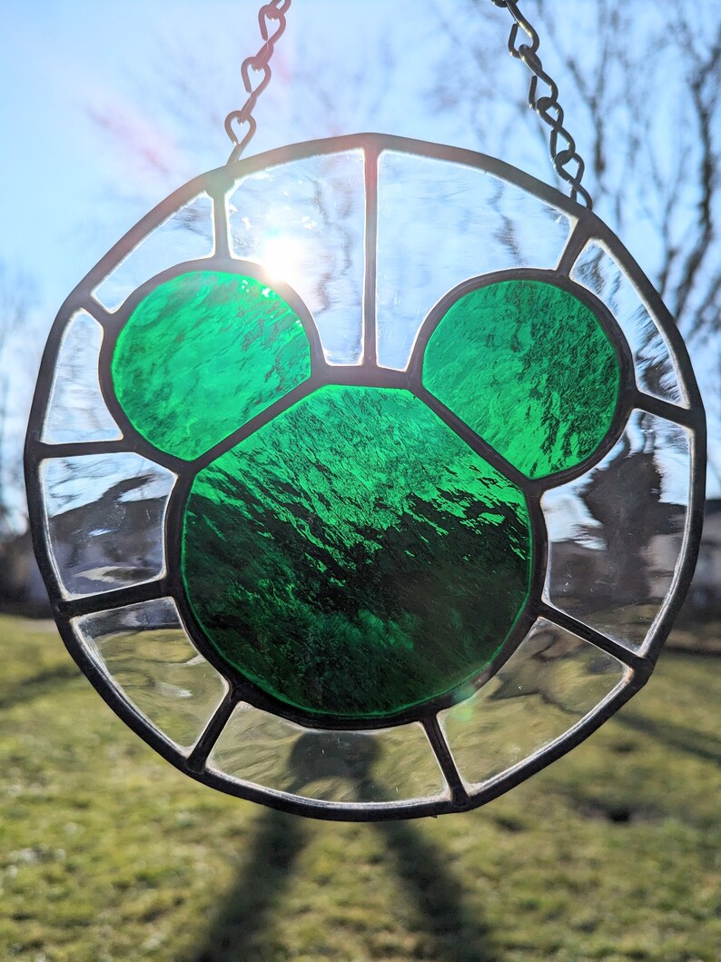 Może przedstawiać: Witrażowe okno wiszące na łańcuchu, przedstawiające zieloną sylwetkę Myszki Miki.