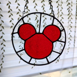 Może przedstawiać: Czerwona głowa Myszki Miki z witrażu wisząca na czarnym łańcuchu. Witraż jest osadzony w okrągłej ramie.
