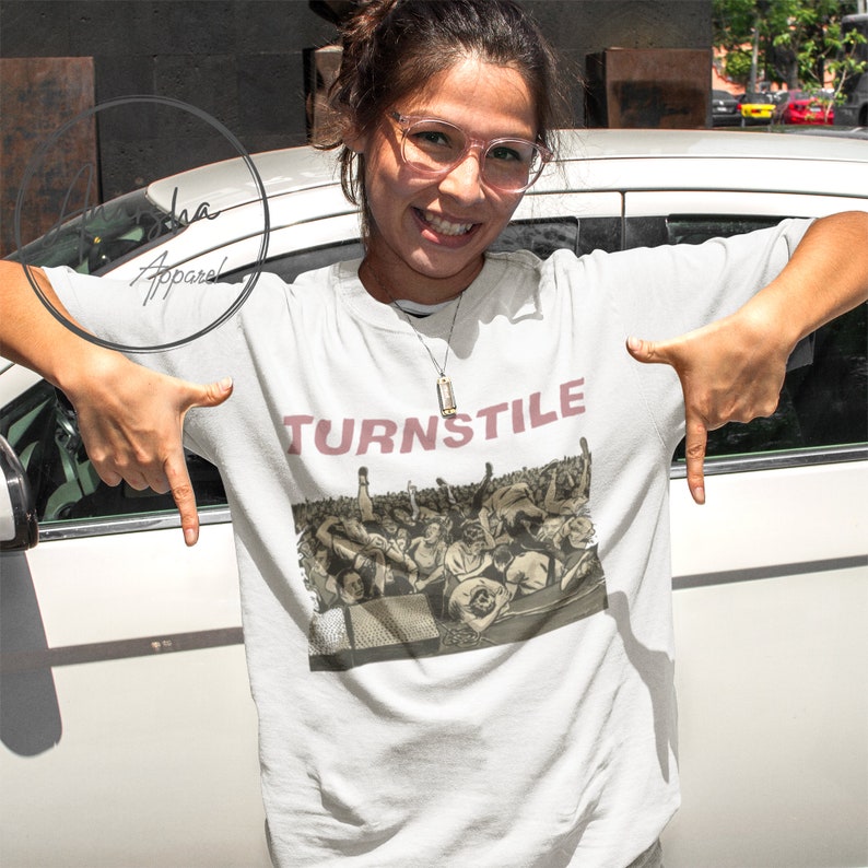 Puede incluir: Camiseta blanca con una imagen en blanco y negro de una multitud en un concierto. El texto "TURNSTILE" est&aacute; impreso en rosa sobre la imagen.