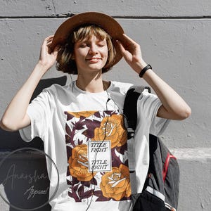 May include: White t-shirt with a floral design featuring orange roses and the text "TITLE FIGHT" in a rectangular box. The shirt is worn with a brown hat and a black backpack.