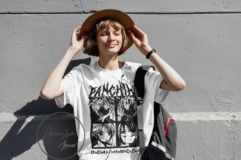 以下が含まれることがあります： 白地に黒と白のアニメ風の顔のグラフィックプリントが施されたTシャツ。顔の上に「FANCHI」という文字が、顔の下に「D>E>A>T>H>M>E>T>A」という文字がプリントされています。