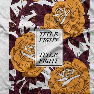 May include: A light gray t-shirt featuring a floral design with large yellow roses and burgundy leaves. The words "TITLE FIGHT" are printed in a white rectangle. The roses have detailed outlines.