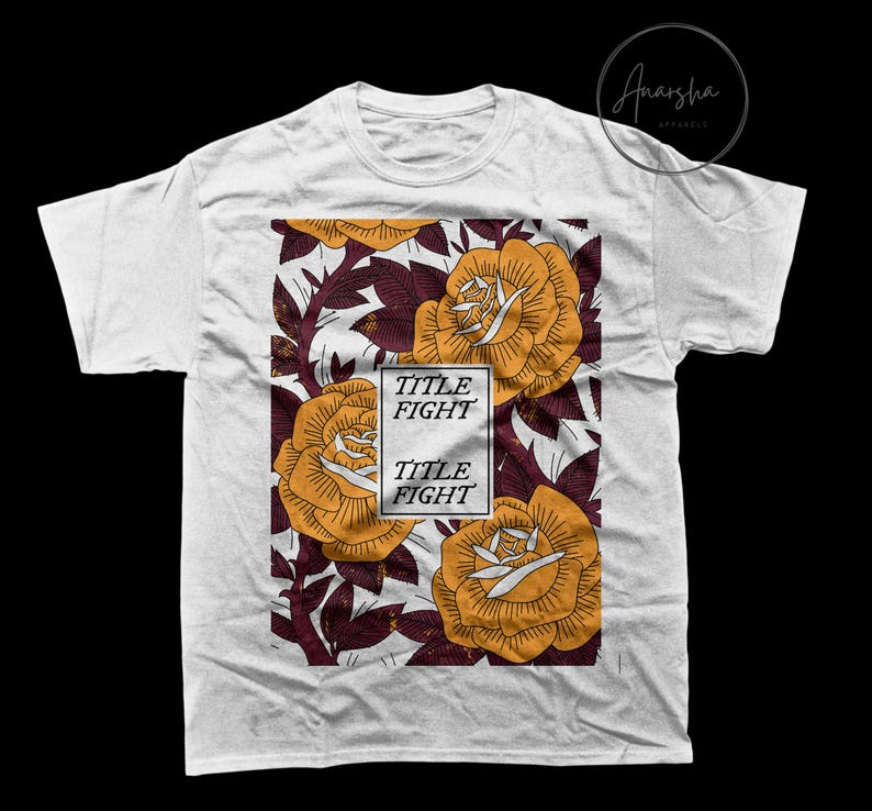 May include: White t-shirt featuring a floral design with large yellow roses and burgundy leaves. The design includes the text "TITLE FIGHT" in a white rectangular box. The shirt is a crew neck style.