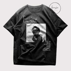 May include: Black t-shirt with a grayscale image of a person, the text "Eversince" above and "Bladee" below. The shirt has a crew neck and short sleeves. The brand name "Anarsha Apparels" is in the upper right corner.