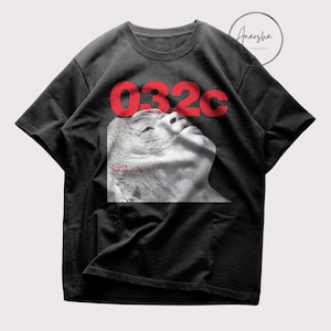 May include: Black t-shirt with the red text "032c" above a grayscale image of a person's face. The text "Ecco2k Debut album "E"" is below the image. The shirt has short sleeves and a crew neck.