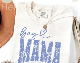 May include: An ivory short-sleeve t-shirt with a crew neckline. The front features the blue text 'Boy' in cursive script next to a heart, and the word 'MAMA' in large blue block letters with white polka dots and small white bow accents.