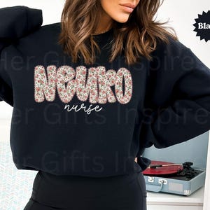 Puede incluir: Sudadera negra de cuello redondo con la palabra "NEURO" en letras grandes con estampado floral y la palabra "nurse" en cursiva. La sudadera es de color negro liso.