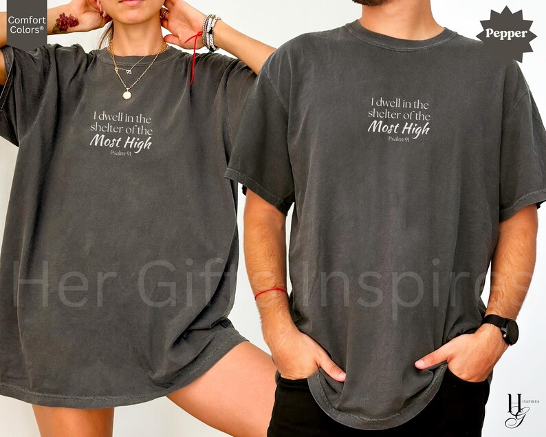May include: A charcoal gray short-sleeve t-shirt featuring the white printed text "I dwell in the shelter of the Most High" followed by "Psalm 91" centered on the chest. The garment has a crew neckline and a relaxed, loose-fitting silhouette.