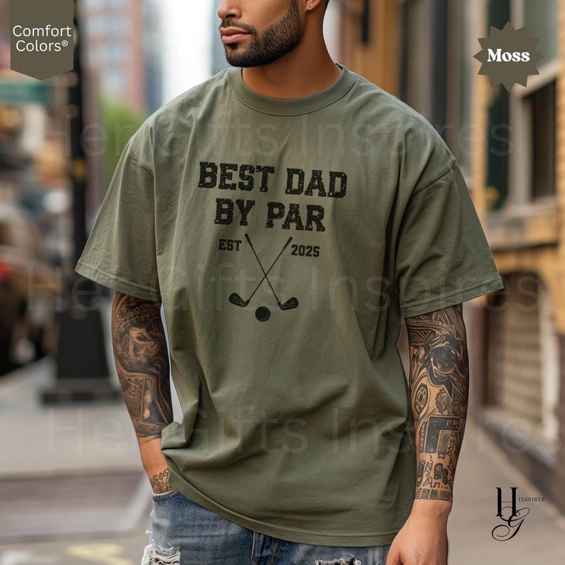 Peut inclure: T-shirt vert mousse Comfort Colors avec l'inscription noire "BEST DAD BY PAR EST 2025". Le motif comprend des clubs de golf crois&eacute;s et une balle. Coupe ample.