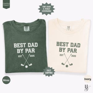 Peut inclure: Deux t-shirts pli&eacute;s, un vert mousse et un ivoire, avec le texte "BEST DAD BY PAR" et des graphiques sur le th&egrave;me du golf. Le texte "EST 2025" est &eacute;galement inclus. Les chemises sont de la marque Comfort Colors.