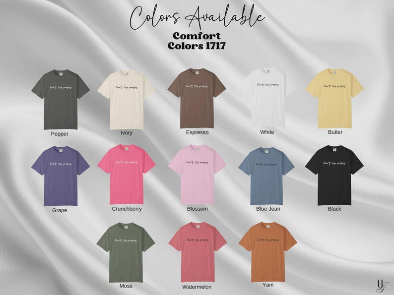 May include: A display of Comfort Colors 1717 t-shirts in various colors, including Pepper, Ivory, Espresso, White, Butter, Grape, Crunchberry, Blossom, Blue Jean, Black, Moss, Watermelon, and Yam. Each shirt has the text "Don't stop praying" printed on the front.