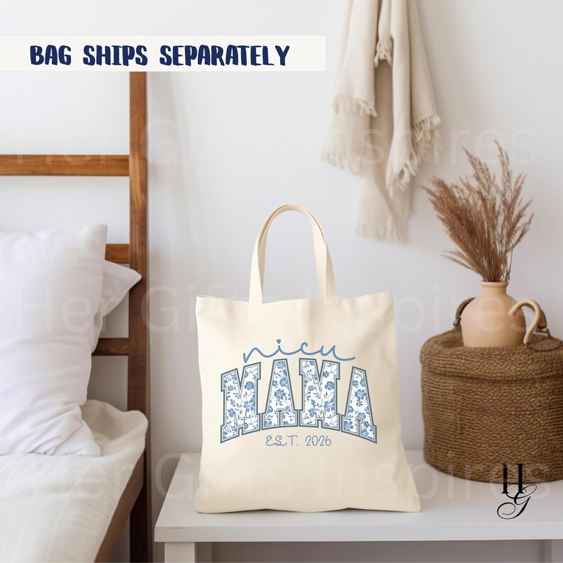 May include: Cream-colored tote bag with the text "nicu MAMA EST. 2026" in blue floral lettering. The bag has two handles and is sitting on a white surface. A decorative vase and basket are in the background.